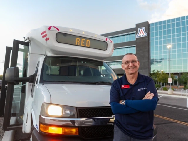 Bill Mason standing outside a Cat Tran shuttle near a building in the background with a Block A logo on it