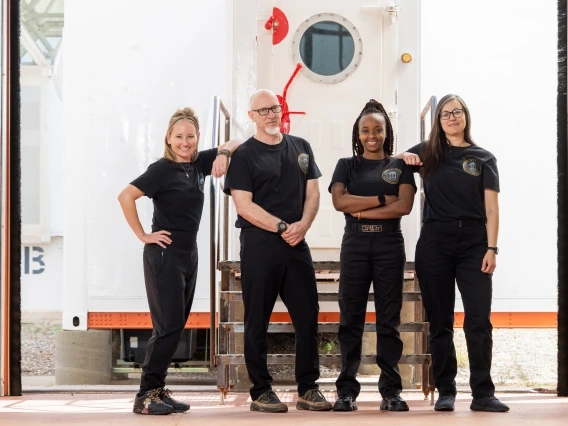 Four people posing in front of an airlock door