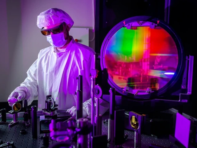 A researcher in a lab coat works on laser technology.