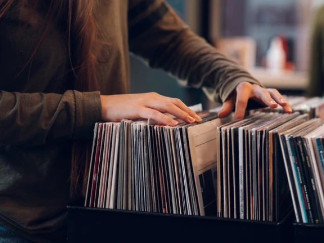 A person flips through a collection of vinyl records in a record store, using both hands to browse the albums in a crate.