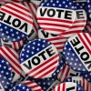 A pile of red, white, and blue "VOTE" buttons featuring stars and stripes, designed to resemble the American flag.